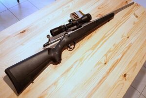 High-precision rifle with scope mounted, resting on a light wooden surface, ideal for accurate shooting and hunting enthusiasts.