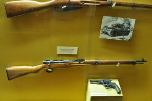 Vintage Japanese Type 99 Carbine rifle and Soviet M1895 revolver displayed in a museum case, highlighting historical firearms used during World War II for educational and collector purposes.