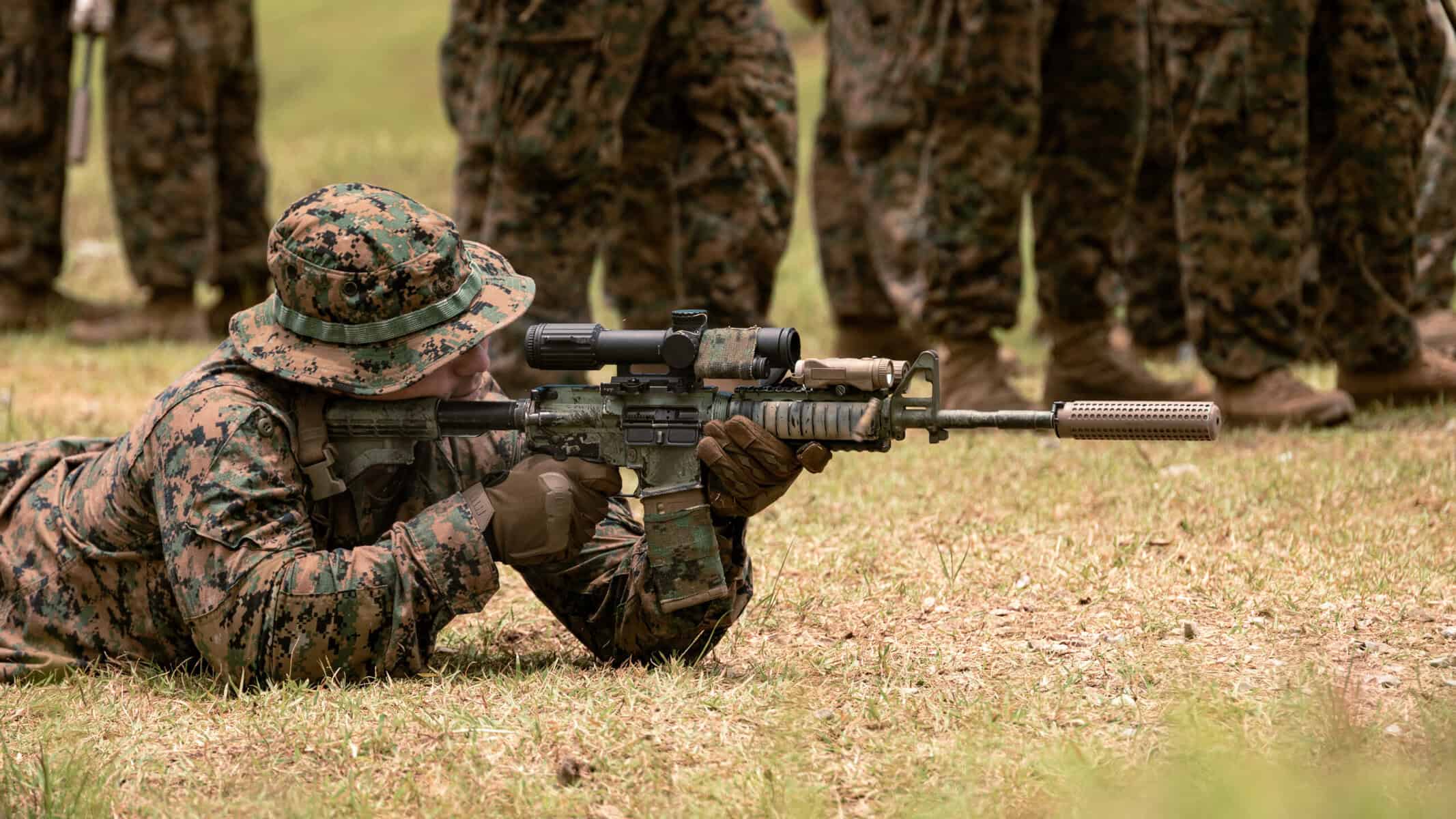 U.S. Marine firing a suppressed rifle at a range — suppressors are standard military equipment now accessible to civilians without the NFA suppressor tax